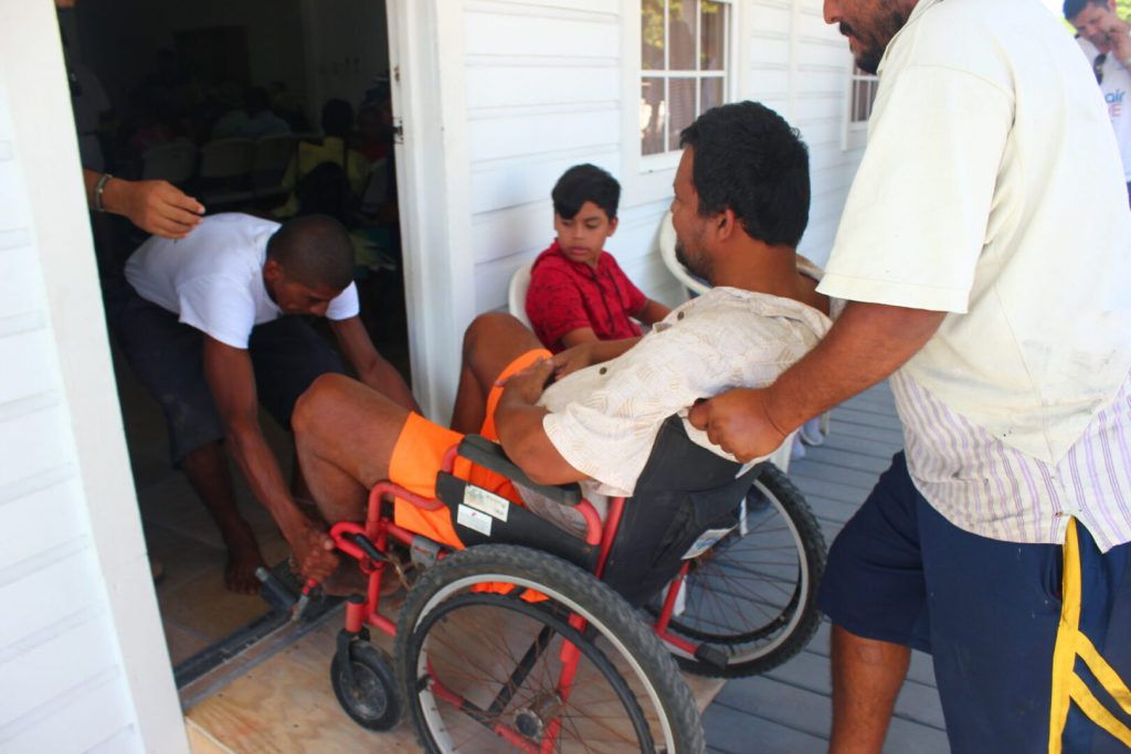Man in a wheel chair helped into a house