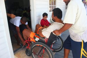 Man in a wheel chair helped into a house